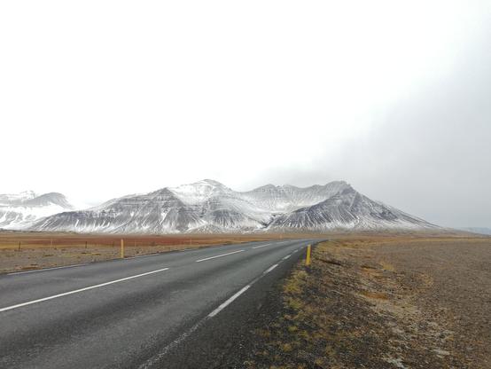 Sous un ciel chargé de nuages se dessine une montagne creusée en son milieu. Une route la longe sur la droite.
