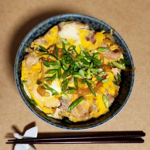 A mottled blue stoneware bowl. Inside is okoyadon. A mix of egg and chicken with onion on a bed of rice. Topped with green onion.