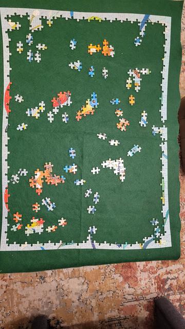 Photo taken from above of a jigsaw puzzle in progress on a green felt background. The frame has been completed and several connected patches appear around the table top.