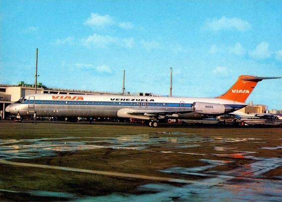 The scene is at the terminal with a parked jet. There are puddles of water on the ground seeming like it just rained.