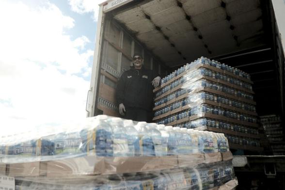 City workers unload a truck containing pallets of bottled water to distribute during a water filter distribution event