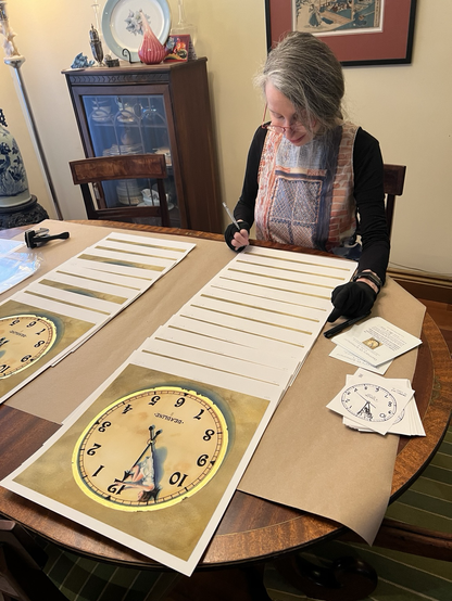 Me (a woman), sitting at a table, with a bunch of prints of my artwork spread out in front of me. The artwork is of my painting, “Deadline”. It features an antique clock-face with a tiny, female figure trapped between the long hand and the shorthand. The rim of the clock is edged in gold leaf. There are about 20 prints of this painting laid out on the table, each one very neatly overlapping the next, and I am signing them and numbering them. I’m wearing black gloves to protect the paper from my fingerprints. It takes a lot of concentration for me to do this task.