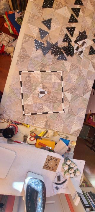 My cutting table and both Time for Tessellation projects laid out. The prototype has the black and white binding and is laying on top the full quilt to, as yet unquilted. There are tools: fabric weights, fabric scissors, paper scissors,chalk liners, steel pins, binding folders, exacto kit, iron, tabletop ironing board, washi tape, coaster (yes fir drinks, I'm a risk taker), and the hackerboxes parts collected for the project.