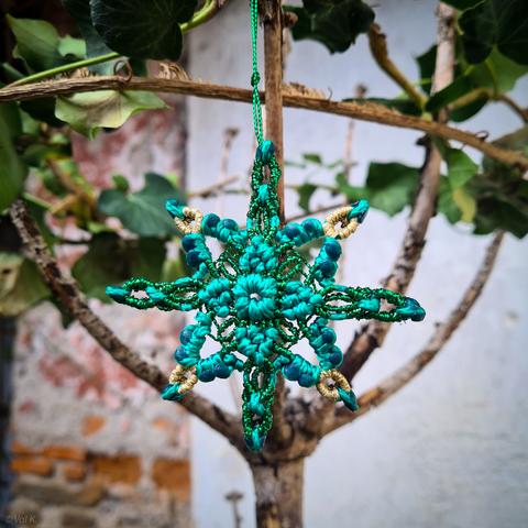 Photo couleur carrée en gros plan. 
Une étoile à 8 branches, 4 petites et 4 grandes, verte et dorée, accrochée à un reste de sapin pimpé avec des du lierre.