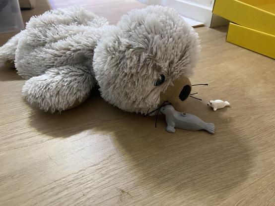 Een zachte grijze zeehondenknuffel op se grond met twee mini plastic lego zeehondjes erbij