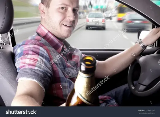 [Shutterstock Stonk Pic]
A white guy driving a car the wrong way on the road hands a beer bottle to us, seated in the passenger seat.