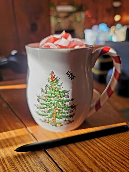 Spode Christmas Mug with candy cane handle filled with hot chocolate and topped with pink peppermint whipped cream. Sitting on a wood table in a secluded cabin deep in the woods of the North Georgia Mountains.