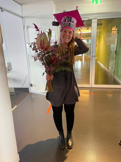 A smiling Lara Wallberg with her PhD hat on and flowers in her hand after the defense.