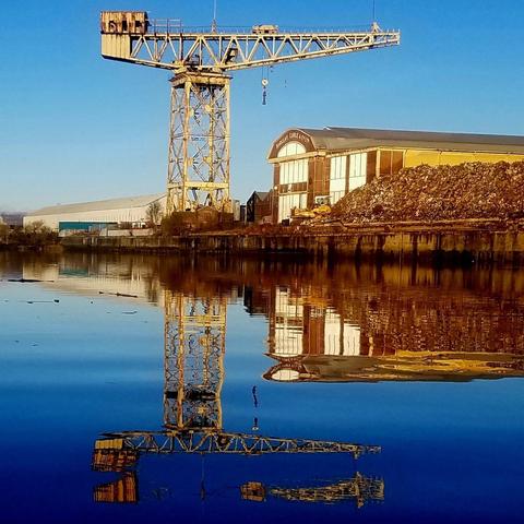 A titan crane stands next to a modernist industrial building on the banks of the Clyde in Glasgow.