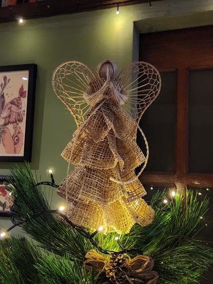 An angel made of natural fibers atop a Christmas tree