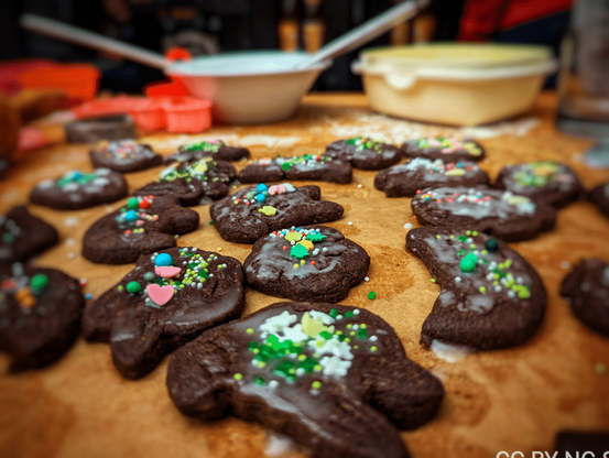 Fertig gebackene und bunt dekorierte Kakaoplätzchen auf Backpapier. Im Hintergrund sind Schüsseln und Ausstechformen zu sehen.

Ready-baked and colorfully decorated cocoa cookies on baking paper. Bowls and cookie cutters can be seen in the background.