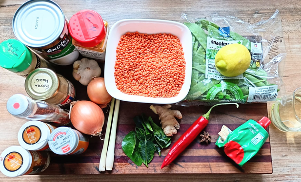 Auf dem Tisch alle Zutaten für die Linsensuppe - rote Linsen,   asiatische Gewürze, Zwiebeln, Chili, Zitronengras, Limettenblätter, Zuckerschoten, Zitrone...