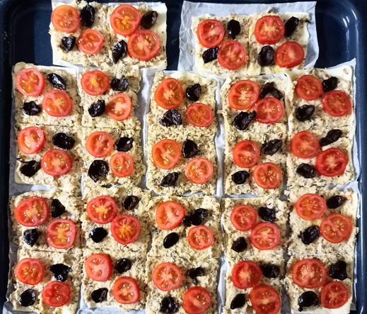 Die fertig belegten Blätterteigstückchen mit Tomate und Olive vor dem Backen auf dem Blech