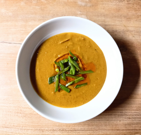 in einer Suppenschale eine glatt pürierte Linsensuppe, in der Mitte Streifen von Zuckerschoten und rötliches Chiliöl