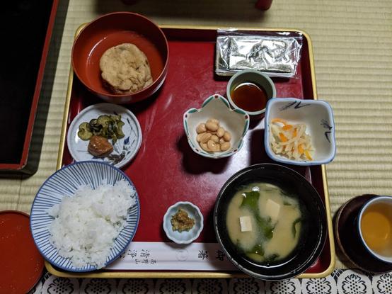 Top view of a tred lacquered tray with many bowls and small dishes with food items - rice, miso soup, pickles, agedashi tofu . A cup with tea is next to the table