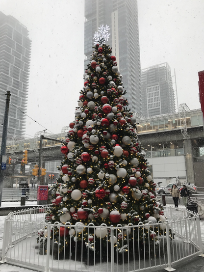 Huge outdoor Christmas tree with red and white baubles. Behind is an MRT station and high-rise condos. All beautifully snow-covered in Burnaby. Pic by Crissy@tech.lgbt