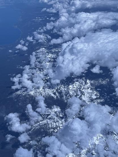 Arial view of mountain ranges and clouds a blue hue sits over the whole picture.