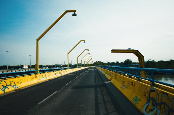 A bridge crossing a river in the outskirts of Vienna. It has been shot standing on the bridge and looking in the direction of the road