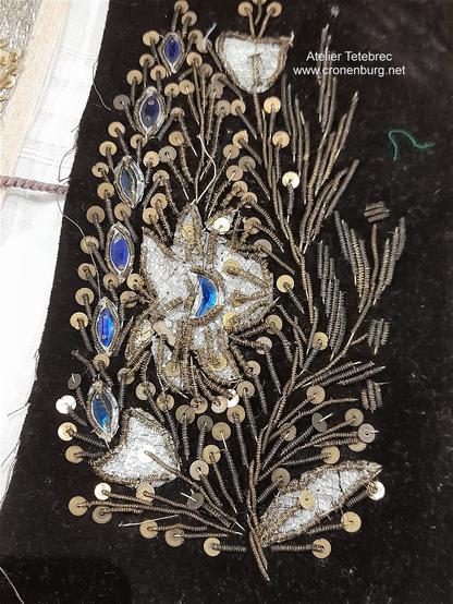 From our museum: Ancient bead embroidery with canetille, sequins, facetted rhinestones and more. It is a floral embroidery in silver and gold with white Flowers on black fabric. Some cobalt-blue rhinestone elements remind peacock feathers.