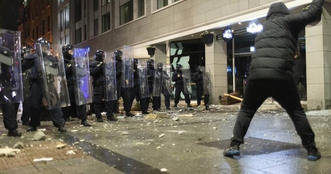 A photograph of a person dressed in black facing off against a row of police behind plastic riot shields. Photograph: Chris Maddaloni