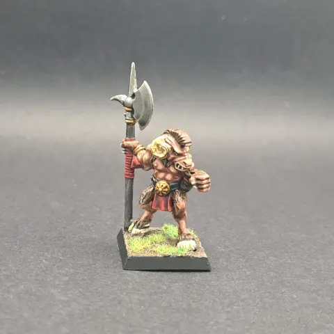 A chaos beastmen model. He has mohawk of brown fur and is only wearing a red loin cloth. He is holding a halberd.