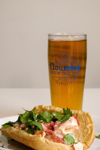 Beer glass filled with beer. Lobster roll on plate.