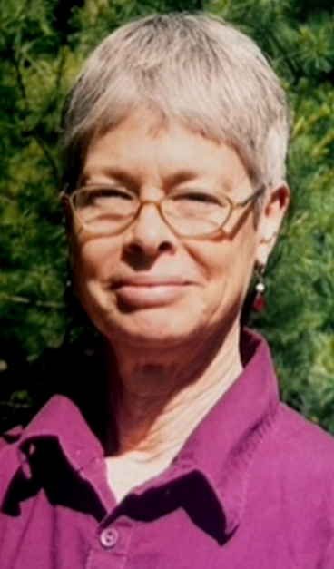 Cecelia Anne Eaton Luschnig, from a 2022 obituary; a white woman with short grey hair, photographed outdoors, wearing glasses and a purple shirt