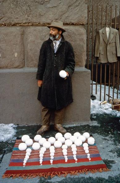 Performance artistique photographiée en couleur par Dawoud Bey. 
L’artiste noir David Hammons se tient debout devant une façade en pierre. 
Il porte un long manteau sombre, un pantalon marron, des souliers usés en cuir brun, des moufles en laine, et est coiffé d’un chapeau.
Il tient dans sa main droite une boule de neige comme s’il la tendait à quelqu’un. 
À ses pieds, il a étalé sur le sol verglacé une couverture à franges rayée aux couleurs vives sur laquelle il a disposé des boules de neige classées par taille, allant de la grosseur d’une boule de pétanque à celle d’une balle de ping-pong. 
À droite de l’image, une haute grille sur laquelle d’autres vendeurs de rue ont suspendu un cintre portant une veste beige et au pied de laquelle gisent des objets abandonnés, comme une canette.