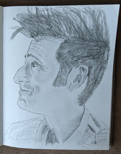 A sketchbook is open to a page featuring David Tennant as the Fourteenth Doctor at the end of the Doctor Who Special, "The Giggle." The Doctor is looking to the left and smiling gently at his newfound family off page. His hair is spikey on top and he's wearing an open collar shirt and plaid vest.