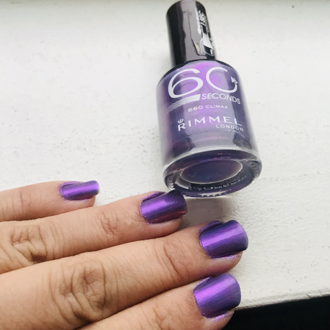 Author showing purple nails against a white table and a bottle of purple nail polish