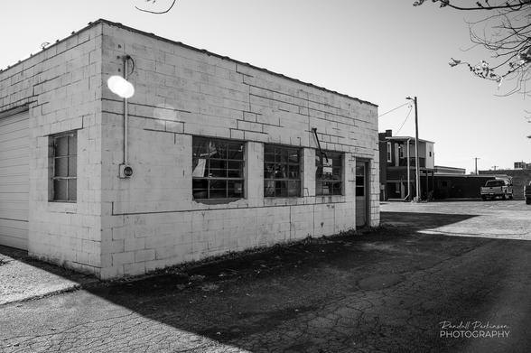 A concrete block building painted white. A garage door and windows are on the left side and 3 windows and a door on the right side.