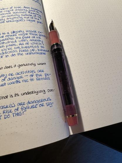 A fountain pen with a clear purple body and opaque pink accents. It has a gold nib.