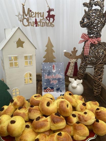 Ein Teller voller Lussekatter vor meinem Buch #Lussekattertage und weihnachtlichem Dekokram.