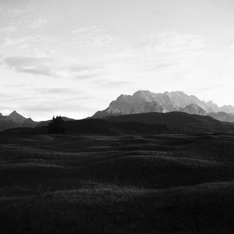 Monochrome photo of bright mountains in the background in the upper part of the image. The lower part shows dark grassland with soft bumps.