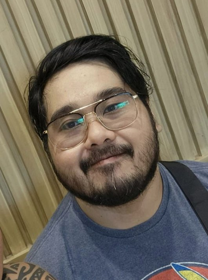 Mark Stephen Florencio smiling casually at the camera. He's wearing big rectangular glasses, is sporting a mustache and shortbeard, brown eyes, and has short black hair parted from his right side. He's Filipino
