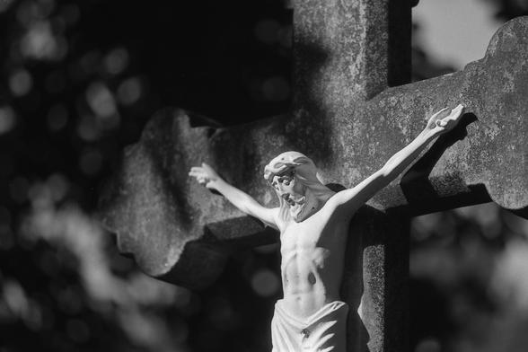 Analoges schwarz-weiß Foto: Ein sehr weißer (marmor?) Jesus hängt an einem Steinkreuz.