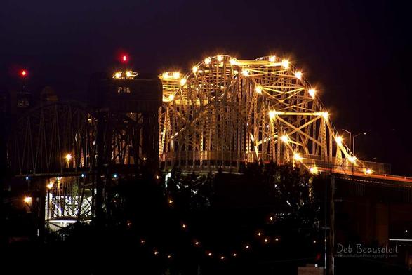 International Bridge between Michigan and Ontario Canada. Image at night, bright lights on the bridge. The railroad bridge is to the left and has 2 red lights at the top. Image at:  https://debbeausoleil.com/2022/01/03/pinpointing-a-specific-date-as-a-turning-point/  See more art at: https://beautifulsunphotography.com/ https://debbeautifulsunphotography.com/ and Blog at  https://debbeausoleil.com