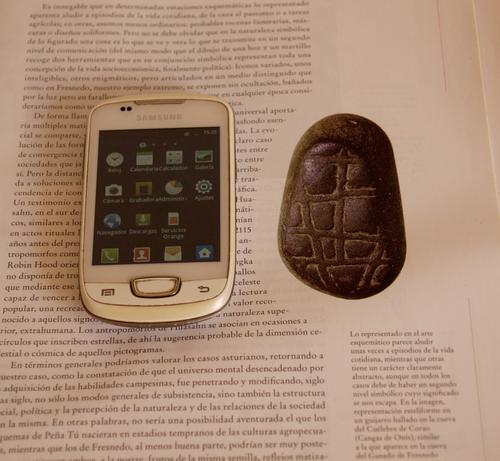 Un teléfono móvil con iconos en pantalla se parece a una piedra del neolítico decorada con motivos geométricos.