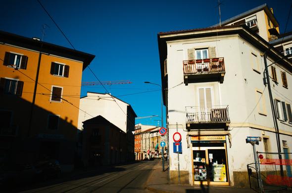 A street with a tramway in the middle in Niguarda neighbourhood in Milan. There are building in both sides, and it is shot with intense shadows/highlights contrast.