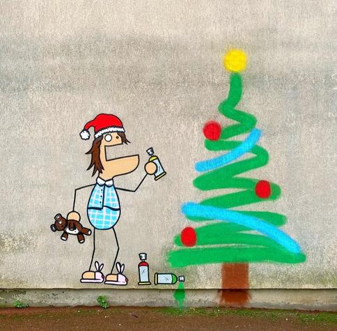 Streetart. A small cartoon figure, spray-painted with simple lines, has drawn a Christmas tree on a gray wall. The little man is wearing a red Christmas hat, short blue and white checked pyjamas and pink slippers. He is holding a teddy bear in one hand and a spray can in the other, with which he has sprayed a Christmas tree with a green wave, a brown line and a few red dots. He hasn't even forgotten the star.
Info: The anonymous artist "TocToc" is a French freelance illustrator and video artist. He exhibits his work in galleries around the world. In 2012, he created the simple figure DUDUSS when he was  an art student and still sprays it on the walls of cities today.