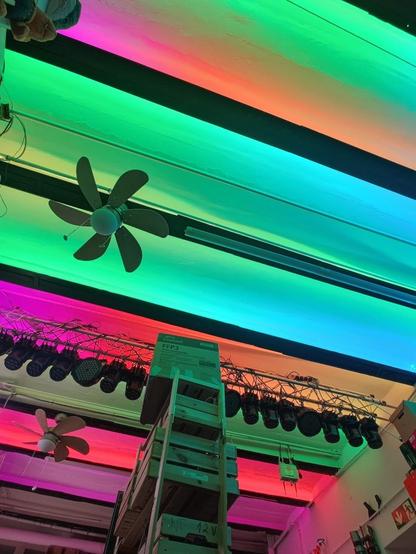 indirekte Deckenbeleuchtung in flauschigen Farben mit 2 Ventilatoren die unter der Decke hängen und eine Traverse wo viele Lampen / Movingheads hängen.