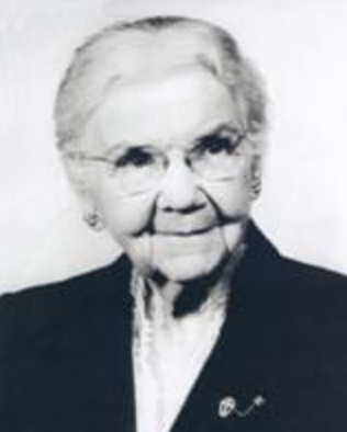 Lelia Judson Tuttle later in life, an older white woman with white hair, wearing glasses and a dark suit jacket