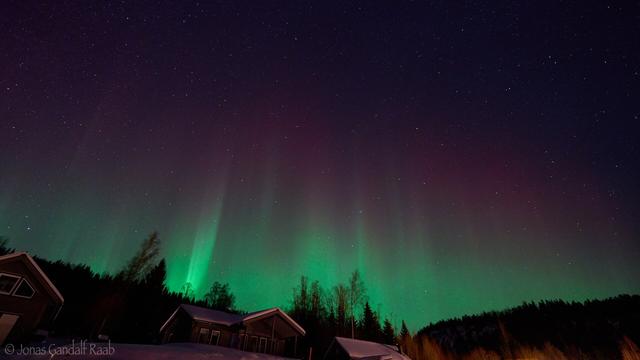 A bright green and purple aurora over a house