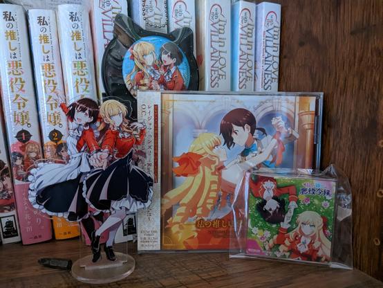 Clair and Rei standee, CD, and two buttons. Manga and novels behind them.