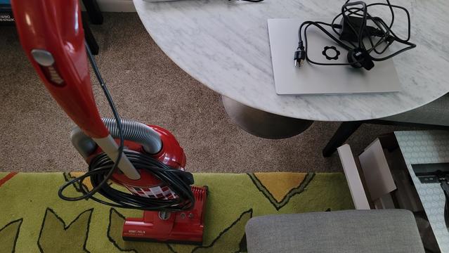 A red SEBO Felix vacuum cleaner standing upright and a Framework Laptop 13 (AMD Ryzen 7) in the field of view.
