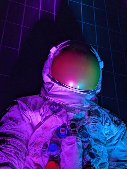A opaque-helmeted space suit, lit from below in garish colors.