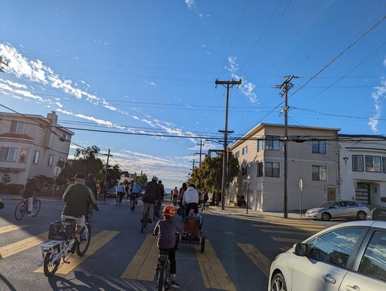 A group of people biking downhill on a sunny day, with the ocean barely visible in the distance