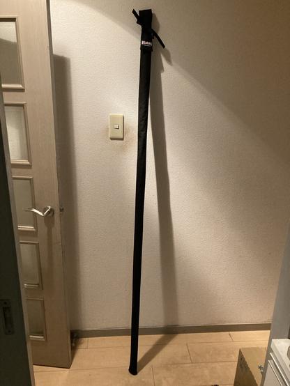 A 182cm long staff holster, back color textile, leaning on a white wall in a house.