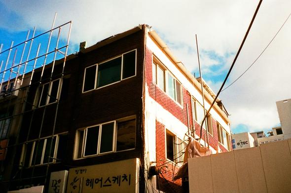 White clouds and blue sky behind the building under construction. Shadow on the left side of the building, sun on the right side.