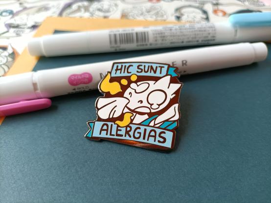 Foto de un pin de dragón alérgico apoyado sobre unos rotuladores